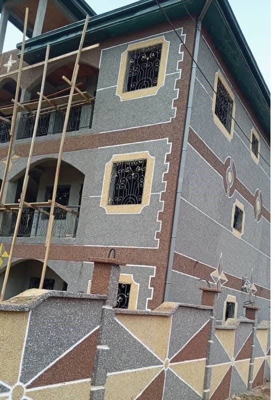 Skilled applicator applying decorative granule wall coating on a Cameroonian home exterior